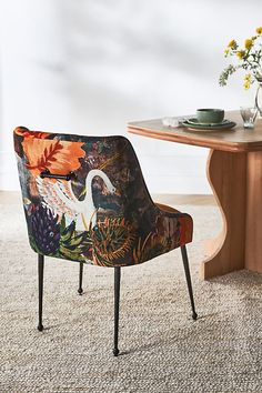 an upholstered chair sits in front of a wooden table with flowers on it