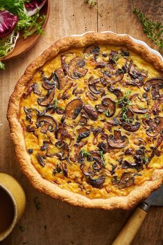 a quiche with mushrooms and herbs on a wooden table next to a bowl of salad