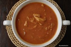 a white bowl filled with red soup on top of a wooden table next to a spoon