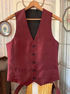 This handsome vest is burgundy with a black sheen/shift on one side and solid black on the other side! It has the original buttons, with three outer pockets on the burgundy side (two of them haven't been opened/unstitched yet) and one chest pocket on the black side. The measurements, taken with the vest lying flat, are: shoulder to shoulder, 12 inches; armpit to armpit, 19 inches; length, 25 1/2 inches in front and 22 inches in back; bottom edge, 17 1/2 inches. In very good condition. Burgundy Vest Outfit Men, Maroon Vest Outfit Men, Sleeveless Business Vest Outerwear, Business Vest With Pockets, Sleeveless Business Vest With Pockets, Formal Winter Sleeveless Vest, Formal Sleeveless Winter Vest, Fitted Solid Vest For Winter, Sleeveless Formal Winter Outerwear