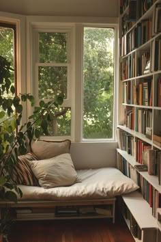 a window seat in front of a bookshelf filled with lots of books and plants