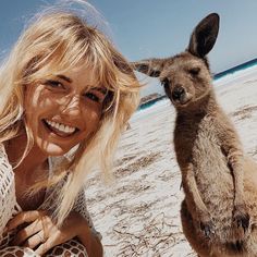 a woman poses for a photo with a kangaroo on the beach in front of her