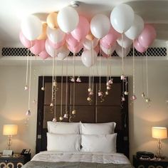 balloons are hanging from the ceiling above a bed with white sheets and pillows on it