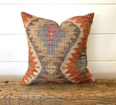 an orange and blue pillow sitting on top of a piece of drift wood next to a white wall