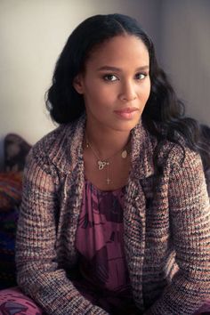 a woman sitting on top of a bed next to a wall and wearing a sweater