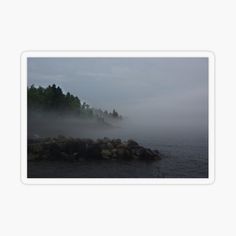 an island in the middle of water with fog covering it and trees on both sides