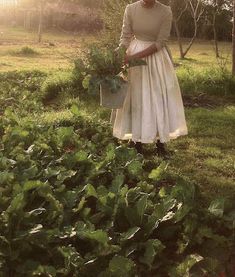 a woman standing in the grass holding a potted plant and wearing a white dress