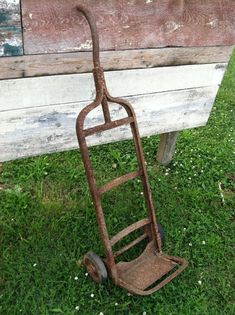 an old rusty hand truck sitting on top of a grass covered field next to a wooden bench