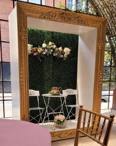 a chair and table in front of a large mirror with flowers on the wall behind it