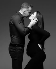 a pregnant couple kissing and posing for a black and white photo with their hands on the belly