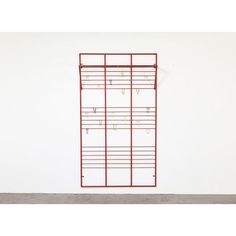 a white wall with a red metal rack on it's side and several pairs of earrings hanging from the hooks