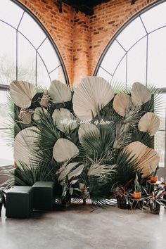 an arrangement of palm leaves and other greenery is displayed in front of large windows