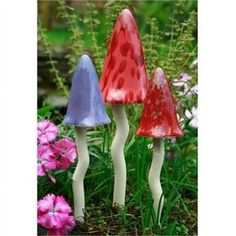 three small plastic mushrooms in the grass with pink flowers behind them and one is red, white, and blue