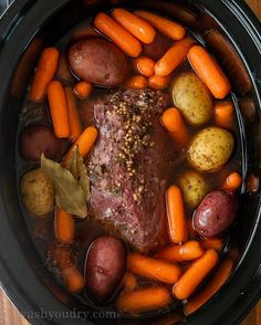 a pot filled with meat, potatoes and carrots next to a wooden table top