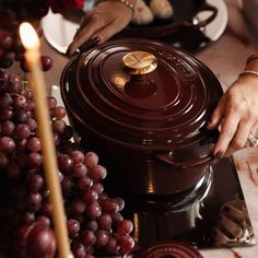 a person placing a candle on top of a chocolate fondant covered dish with grapes