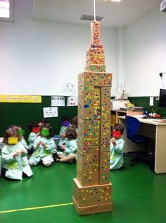 a group of children sitting on the floor in front of a building made out of blocks