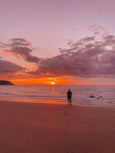 a person standing on top of a beach next to the ocean under a cloudy sky