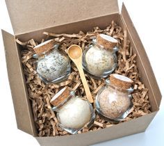 an open box with four different types of bath salts and a wooden spoon in it