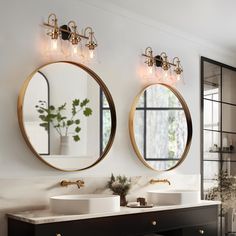 two round mirrors hanging on the side of a wall next to sinks in a bathroom