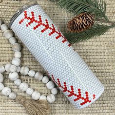 a white can with red letters on it sitting next to some beads and pine cones