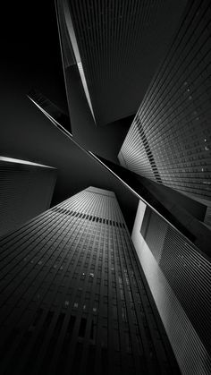 black and white photograph of tall buildings in the city at night, looking up into the sky