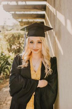 a woman wearing a graduation cap and gown leaning against a wall with her arms crossed