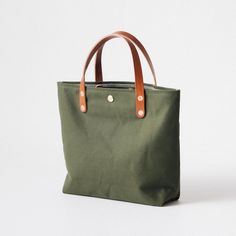 The Green Canvas mini tote is a canvas and leather tote handmade in the KMM & Co. studio in Atlanta. Each one is meticulously crafted from heavyweight canvas and gorgeous full-grain leather. Green Canvas is a type of cotton canvas known as duck cloth. It's one of the most durable types of cloth, and it's structured enough to stand up on its own. The Green Canvas mini tote comes standard with Tan handles. Khaki Canvas Tote Bag With Leather Handles, Everyday Khaki Duck Canvas Bag, Khaki Canvas Bag With Handles, Khaki Leather Bag For Everyday Use, Khaki Canvas Bag, Everyday Khaki Leather Canvas Bag, Everyday Canvas Bag With Rolled Handles, Everyday Top Handle Canvas Bag, Everyday Canvas Shoulder Bag With Rolled Handles