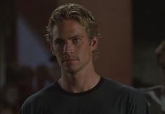 a man with blonde hair and black shirt looking at the camera while standing in a dark room