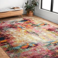 a colorful area rug with an abstract design in the middle and a plant next to it