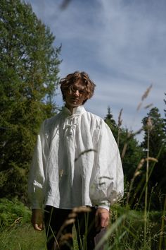 a man standing in tall grass wearing a white shirt