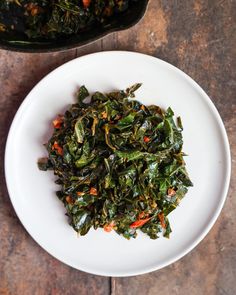 a white plate topped with cooked greens next to a pan