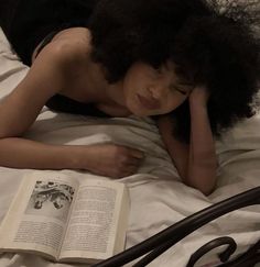 a woman laying on top of a bed next to an open book in her hand