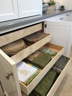 an open drawer in a kitchen filled with folded cloths and place mats on the floor