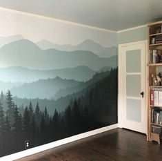 a room with a book shelf and painted mountain scene on the wall next to a bookshelf