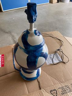 a blue and white vase sitting on top of a cardboard box next to a power cord