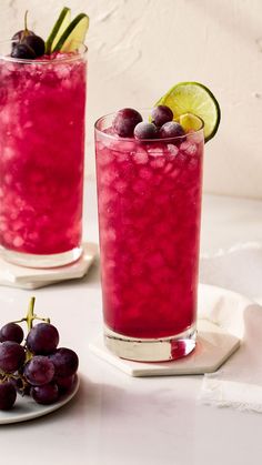 two glasses filled with fruit and garnish sitting on a white table next to each other