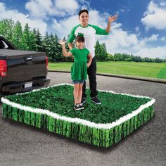 a man and child standing on top of a fake grass field in front of a truck