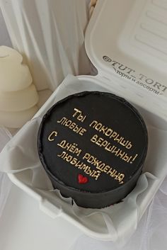 a cake in a box with writing on the side and a candle next to it