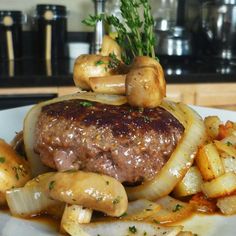 a white plate topped with meat covered in gravy next to potatoes and mushrooms