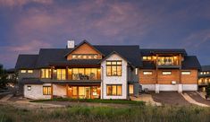 a large house with lots of windows and lights on it's front porch at dusk