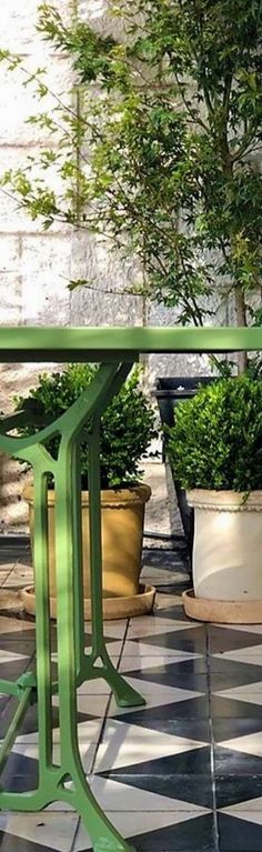 a green table sitting on top of a black and white checkered floor next to potted plants