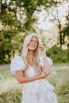 a woman in a white dress smiling and posing for the camera with her hand on her cheek