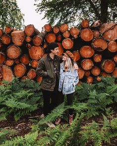 a man and woman standing next to each other in front of a pile of logs