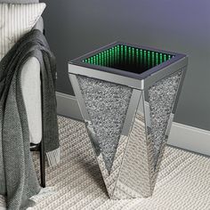 a silver metal planter with green lights in the center on carpeted floor next to bed