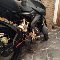 a black motorcycle parked on top of a stone floor next to a brick wall and door