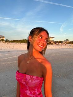 a woman in a pink dress standing on the beach