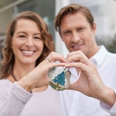 a man and woman making a heart shape with their hands while holding a small ornament