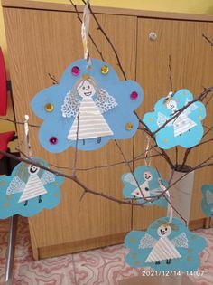 a tree decorated with blue and white paper angel decorations on it's branches in front of a wooden cabinet