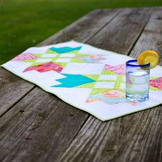 a quilted table runner with an orange slice on it and a glass of water