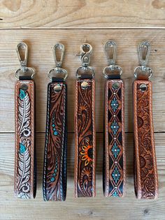 four leather key fobs are lined up on a wooden surface